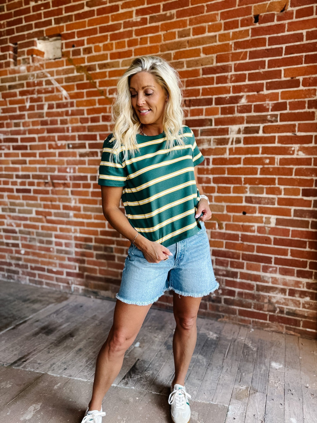 A woman wearing a green and yellow striped short sleeve top with a relaxed fit, standing against a stone wall.