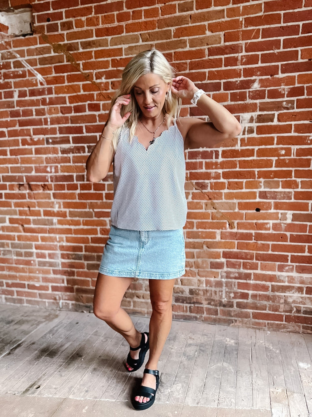 A woman wearing a black polka dot cami tank top with scalloped neckline and adjustable straps.