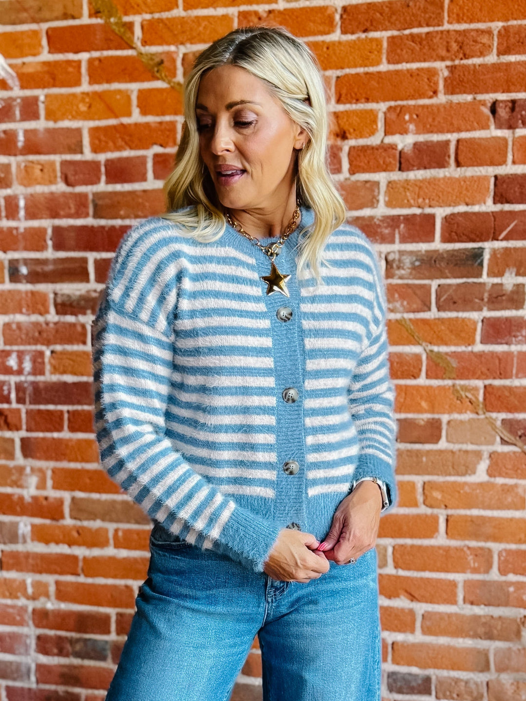 A woman wearing a striped fuzzy cardigan in dusty blue and white, buttoned up with ribbed hem and cuffs.