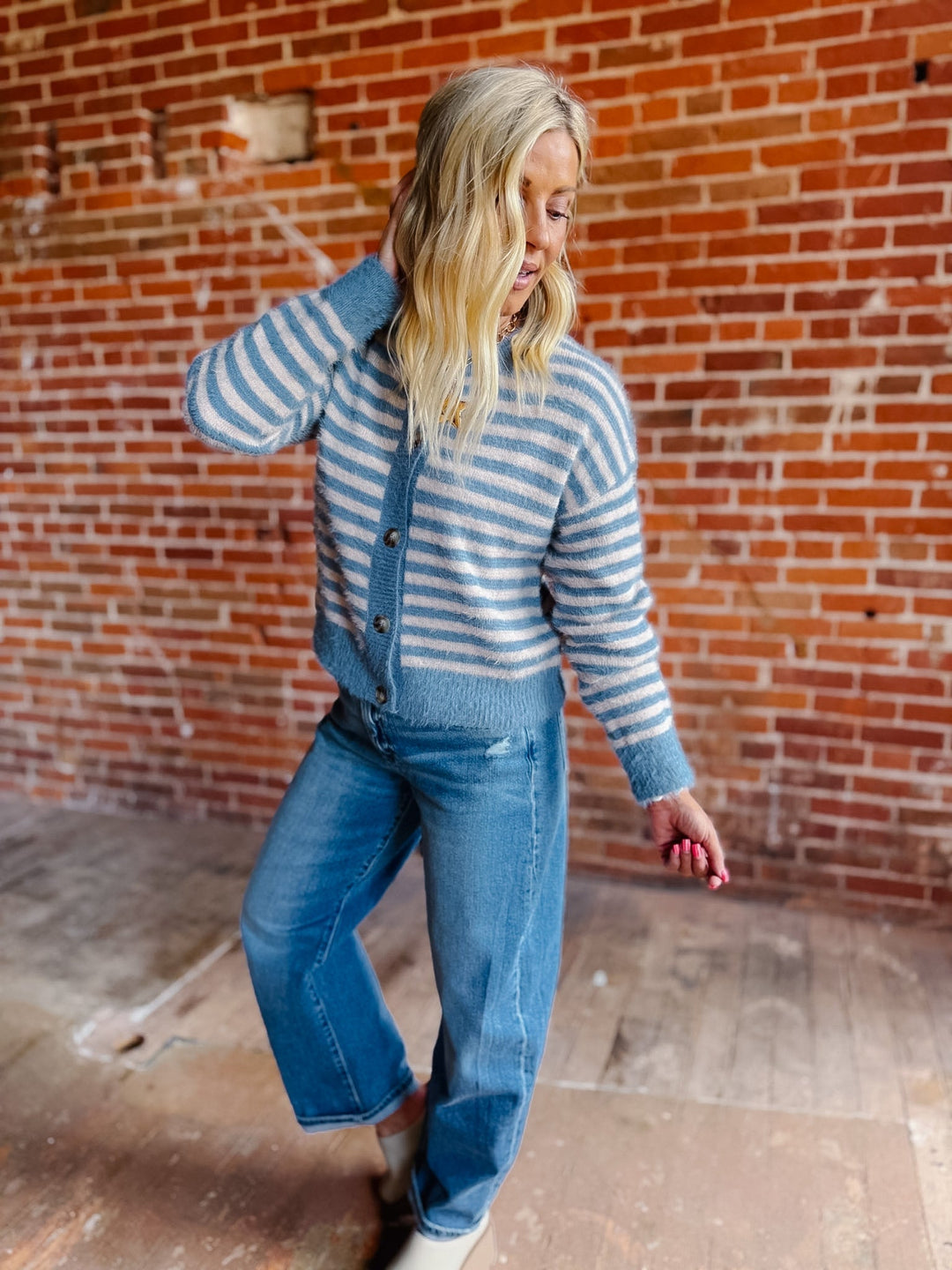 A woman wearing a striped fuzzy cardigan in dusty blue and white, buttoned up with ribbed hem and cuffs.