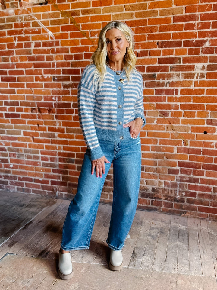 A woman wearing a striped fuzzy cardigan in dusty blue and white, buttoned up with ribbed hem and cuffs.