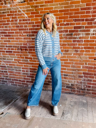 A woman wearing a striped fuzzy cardigan in dusty blue and white, buttoned up with ribbed hem and cuffs.