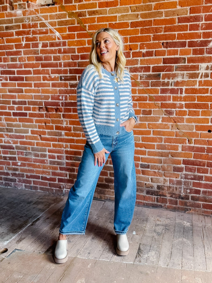A woman wearing a striped fuzzy cardigan in dusty blue and white, buttoned up with ribbed hem and cuffs.