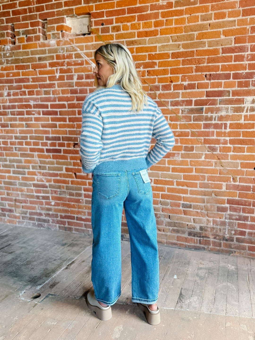 A woman wearing a striped fuzzy cardigan in dusty blue and white, buttoned up with ribbed hem and cuffs.