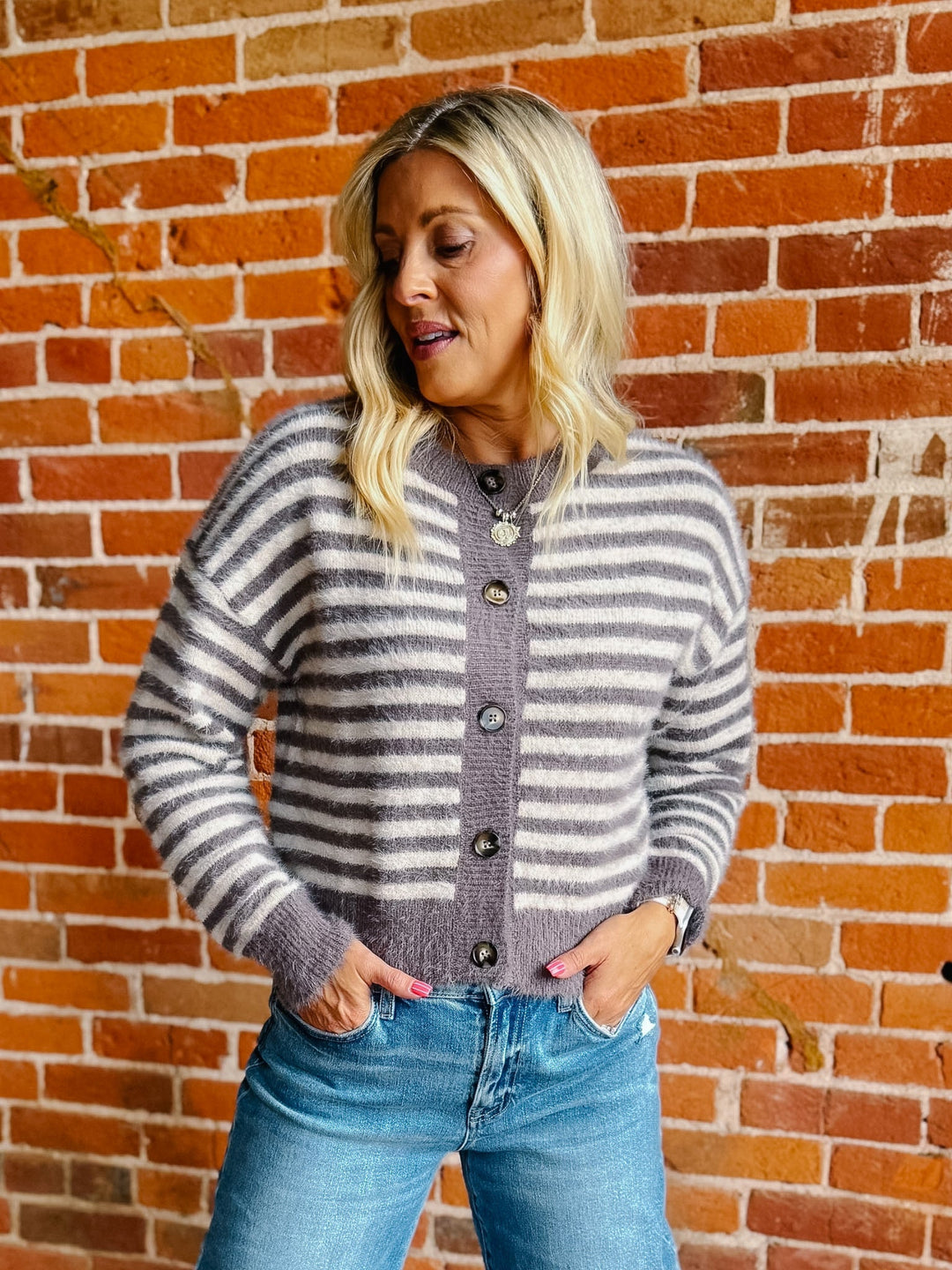 A woman wearing a striped fuzzy cardigan in mocha and white, buttoned up with ribbed hem and cuffs.