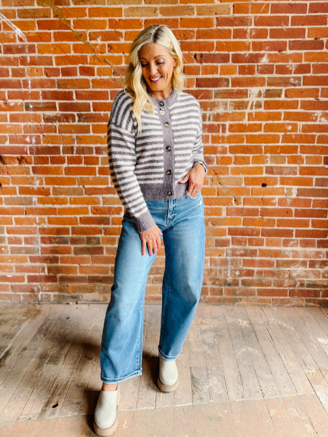 A woman wearing a striped fuzzy cardigan in mocha and white, buttoned up with ribbed hem and cuffs.