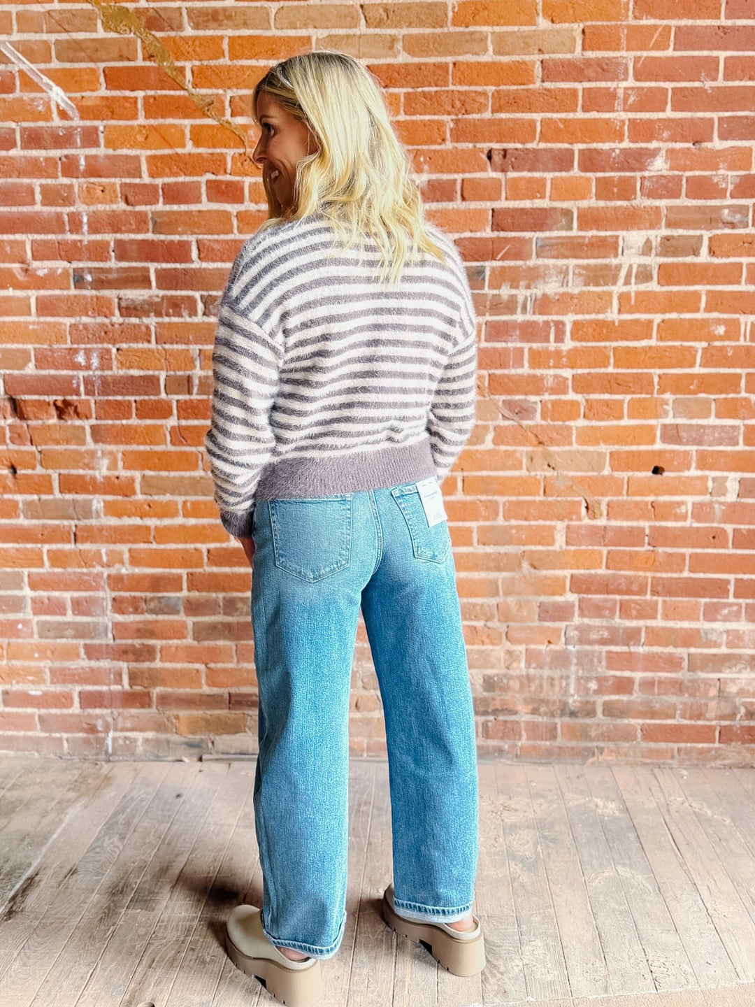 A woman wearing a striped fuzzy cardigan in mocha and white, buttoned up with ribbed hem and cuffs.