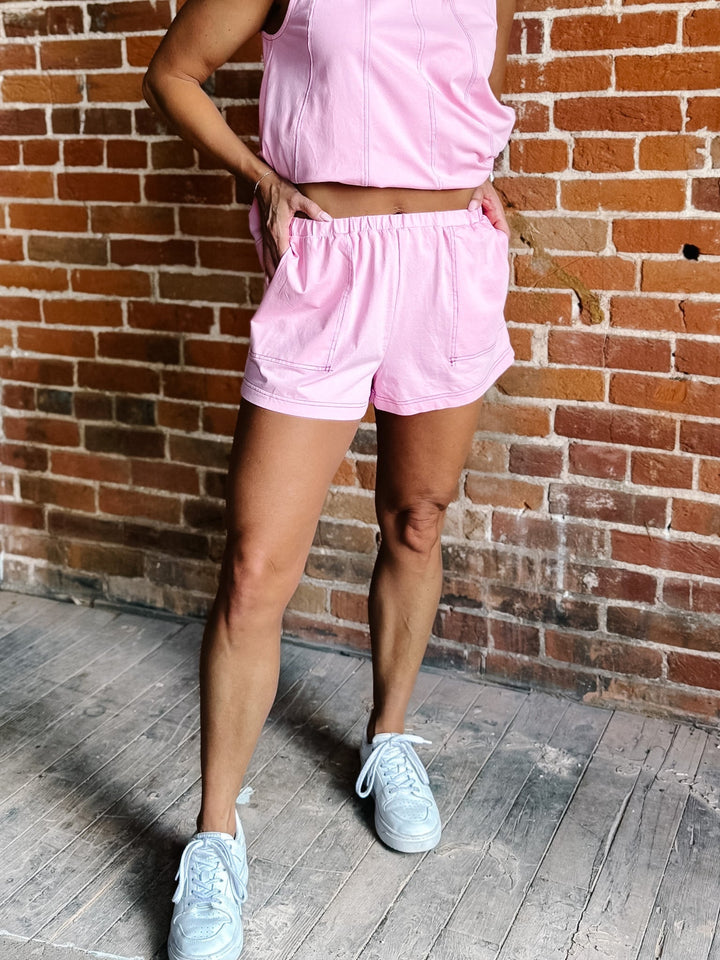 Woman wearing Soft Drift Lounge Shorts in Sweet Pink standing against a brick wall.