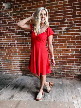 A woman wearing a red fit-and-flare dress with flutter sleeves and a V-neckline.
