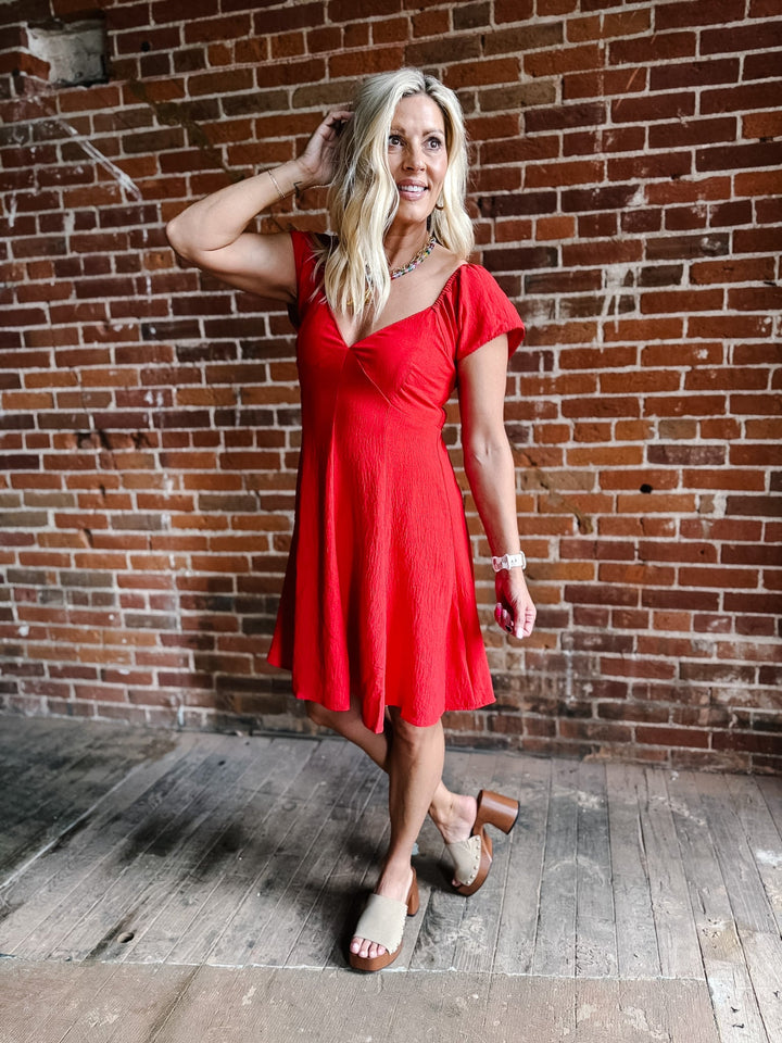 A woman wearing a red fit-and-flare dress with flutter sleeves and a V-neckline.