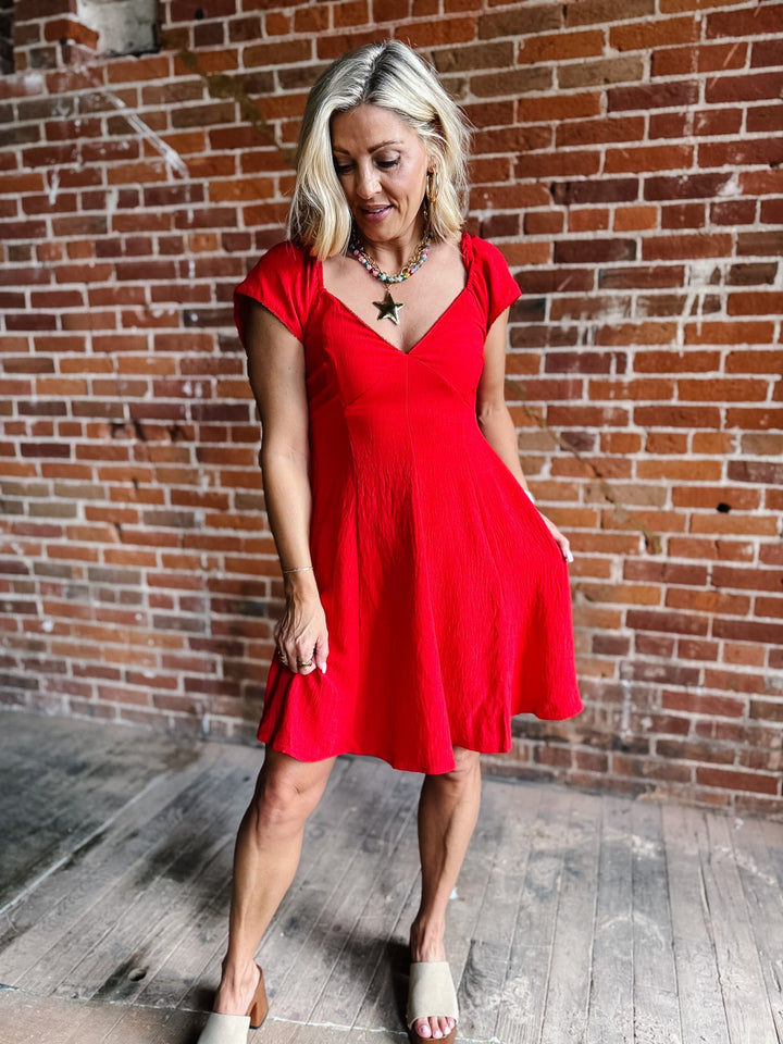A woman wearing a red fit-and-flare dress with flutter sleeves and a V-neckline.