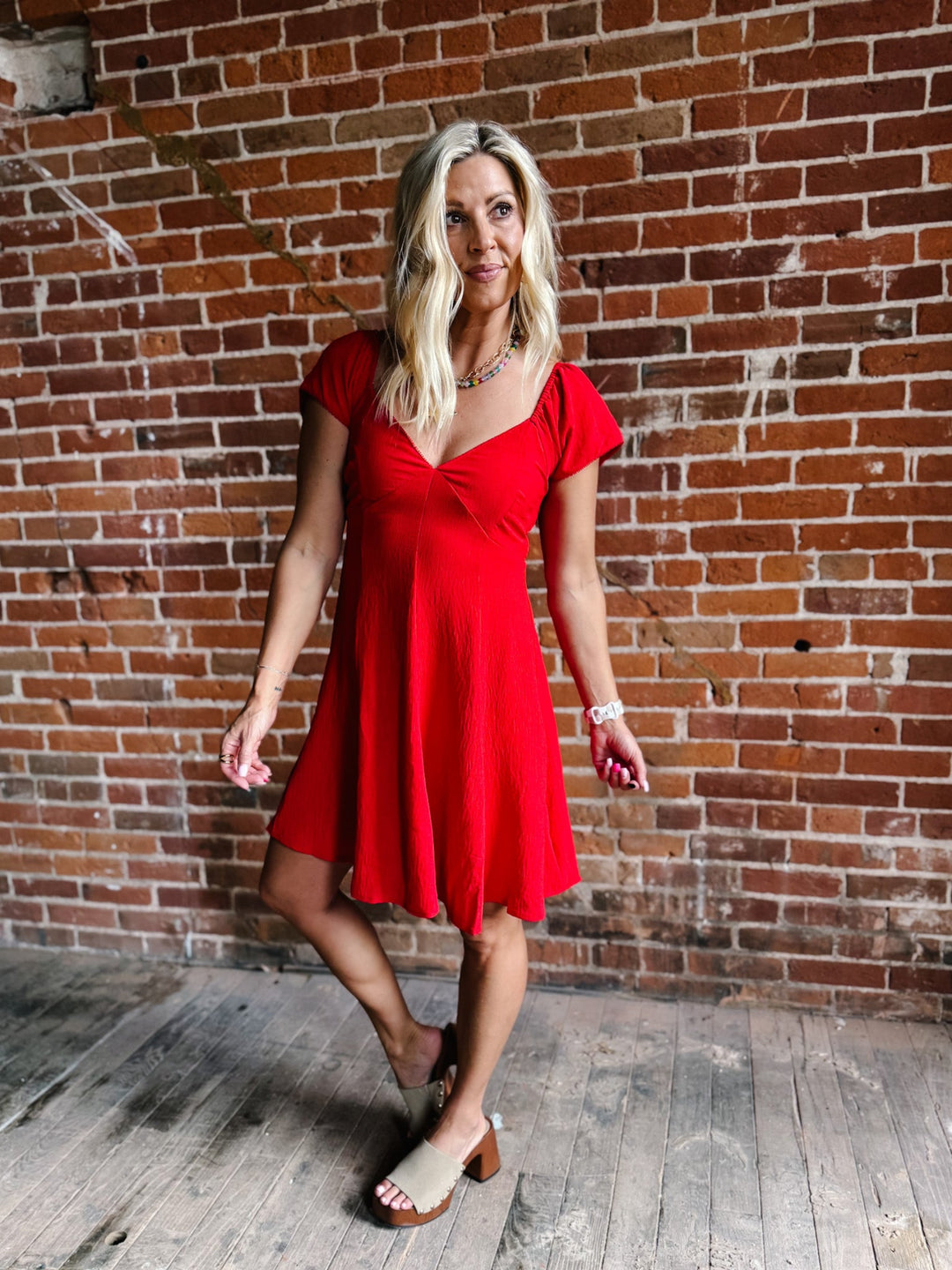 A woman wearing a red fit-and-flare dress with flutter sleeves and a V-neckline.