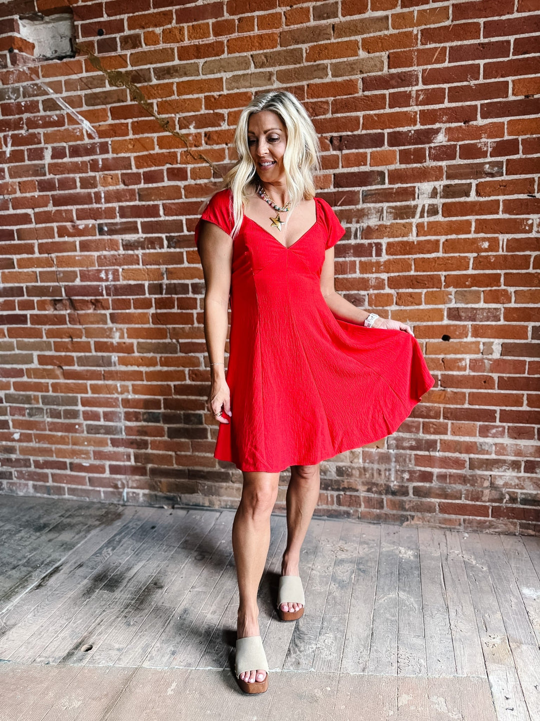 A woman wearing a red fit-and-flare dress with flutter sleeves and a V-neckline.