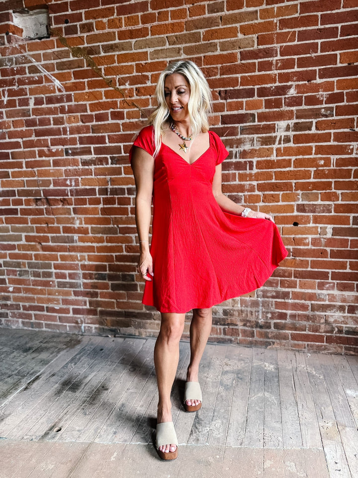 A woman wearing a red fit-and-flare dress with flutter sleeves and a V-neckline.