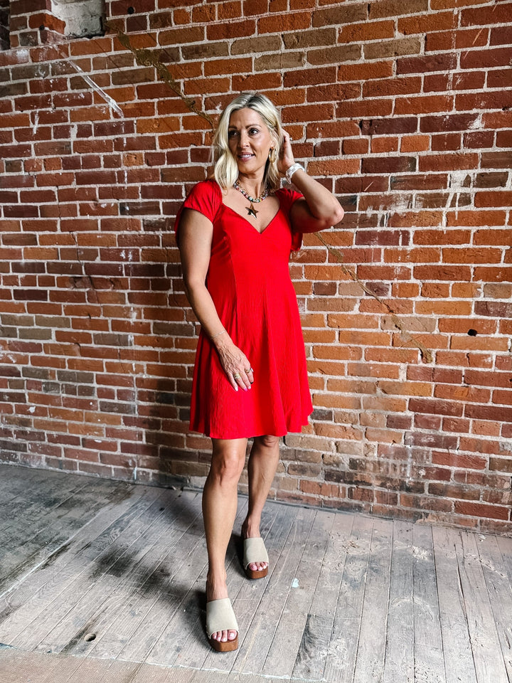 A woman wearing a red fit-and-flare dress with flutter sleeves and a V-neckline.