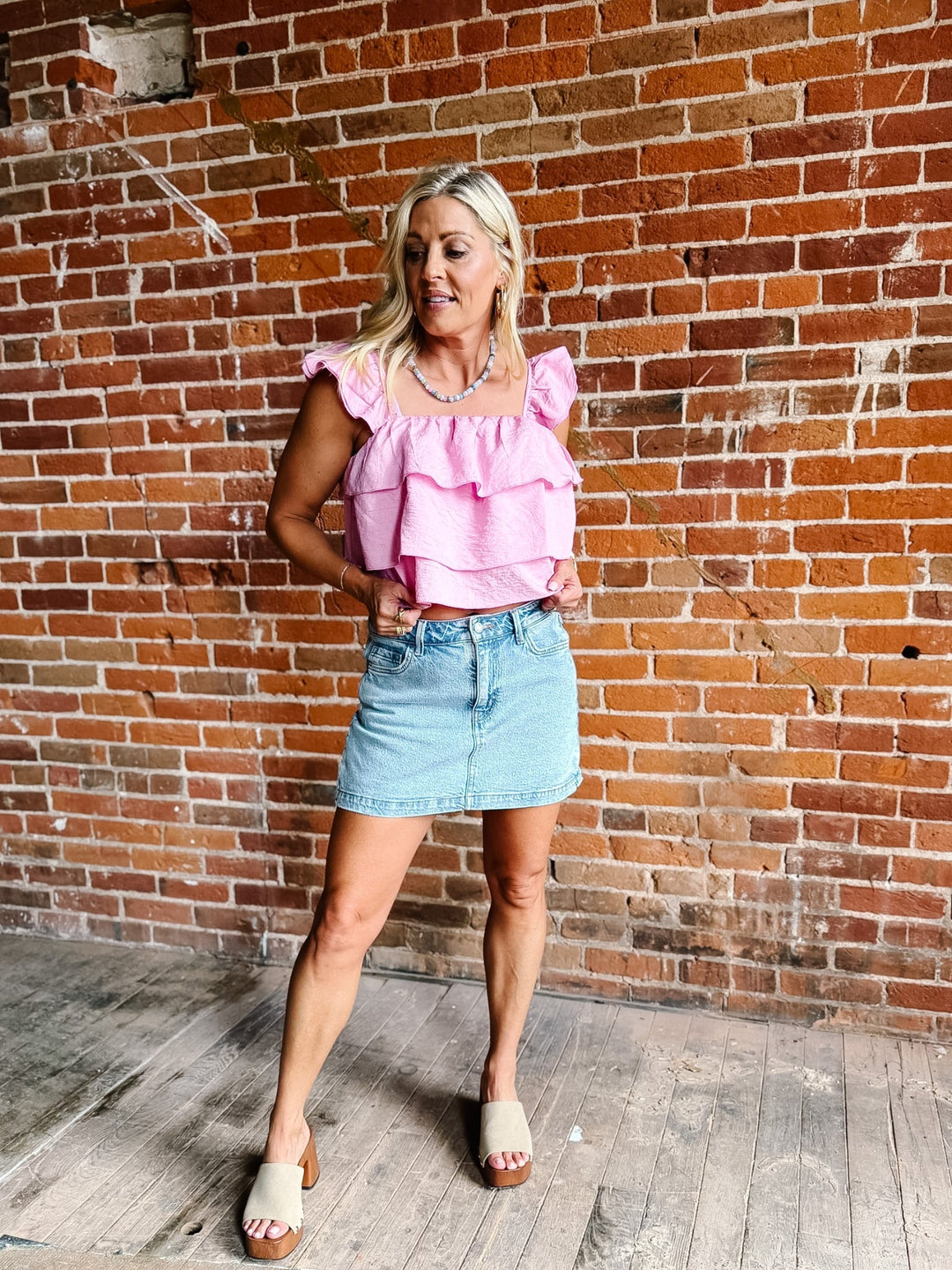 Woman wearing a pink tank top with triple-tiered ruffles and flutter sleeves, paired with a denim skirt.