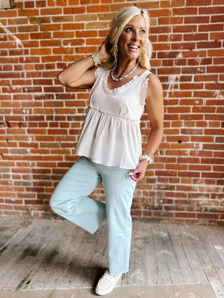 A woman wearing a sleeveless, V-neck ruffle tank in light cotton with a flowy babydoll silhouette.