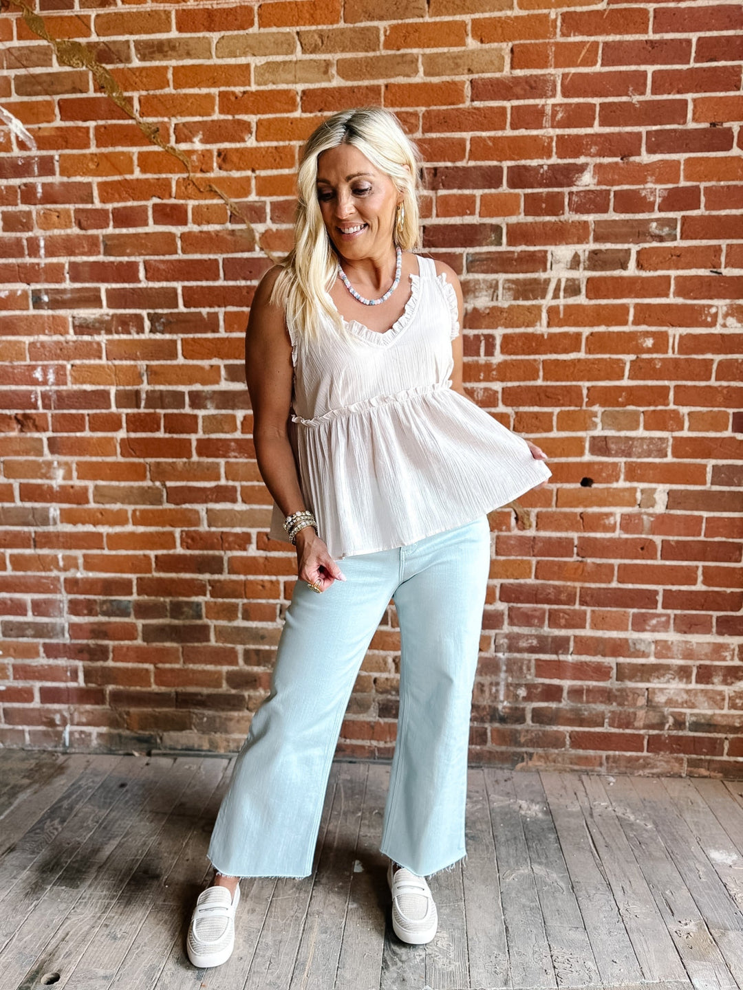 A woman wearing a sleeveless, V-neck ruffle tank in light cotton with a flowy babydoll silhouette.