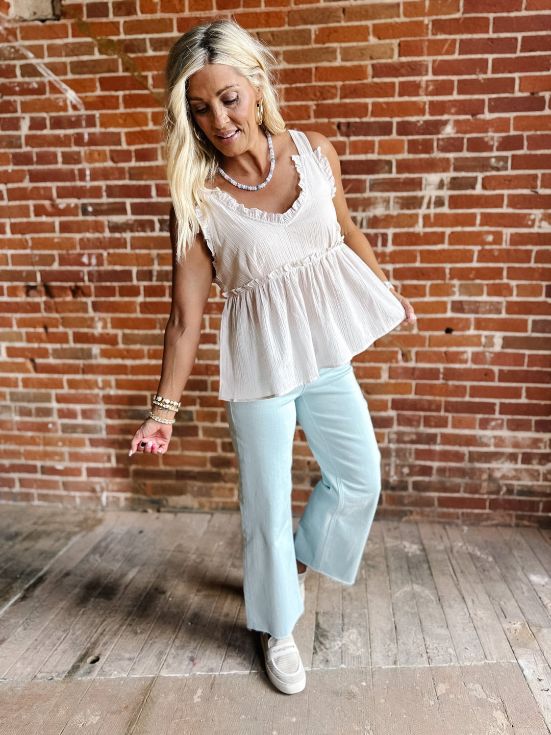 A woman wearing a sleeveless, V-neck ruffle tank in light cotton with a flowy babydoll silhouette.