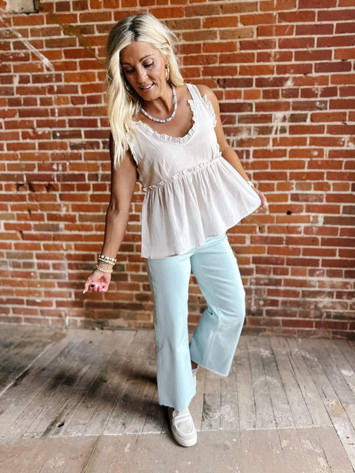 A woman wearing a sleeveless, V-neck ruffle tank in light cotton with a flowy babydoll silhouette.