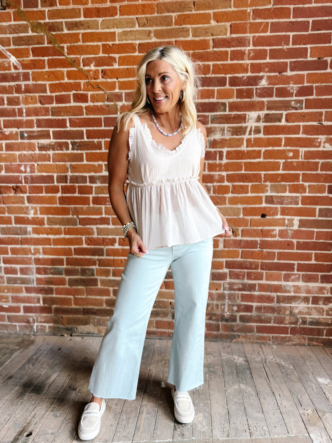 A woman wearing a sleeveless, V-neck ruffle tank in light cotton with a flowy babydoll silhouette.