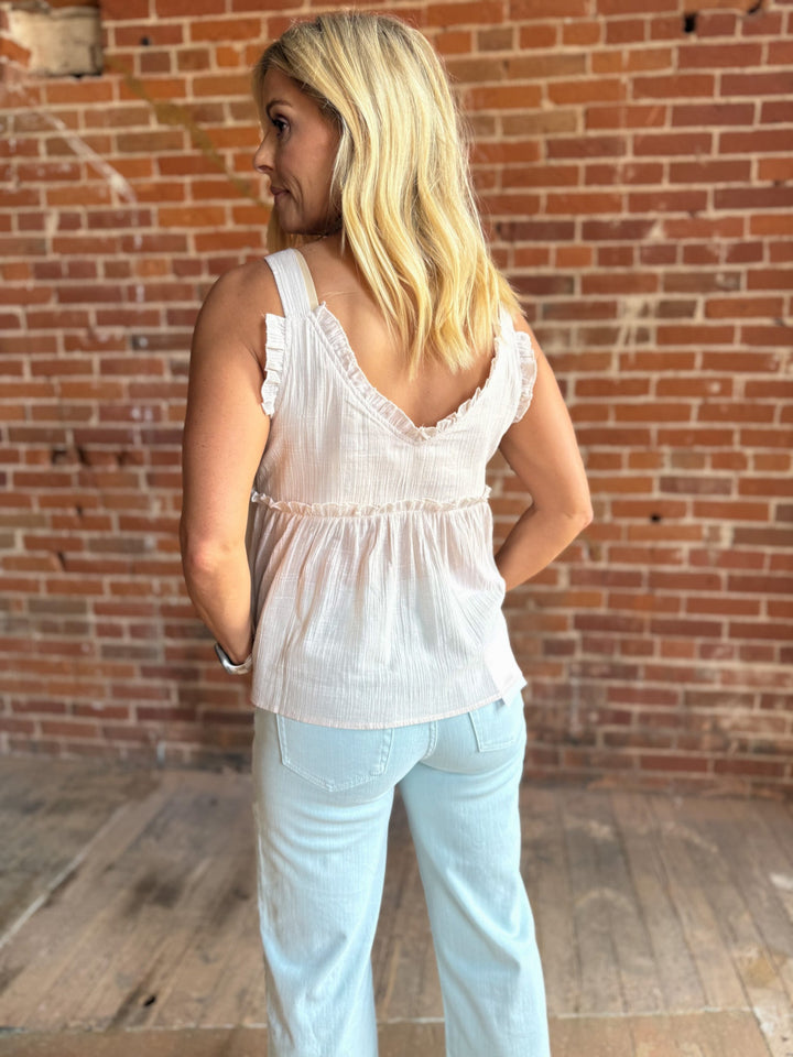 A woman wearing a sleeveless, V-neck ruffle tank in light cotton with a flowy babydoll silhouette.