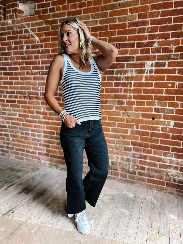 Woman wearing a white and black reversible stripe tank top, standing against a brick wall.