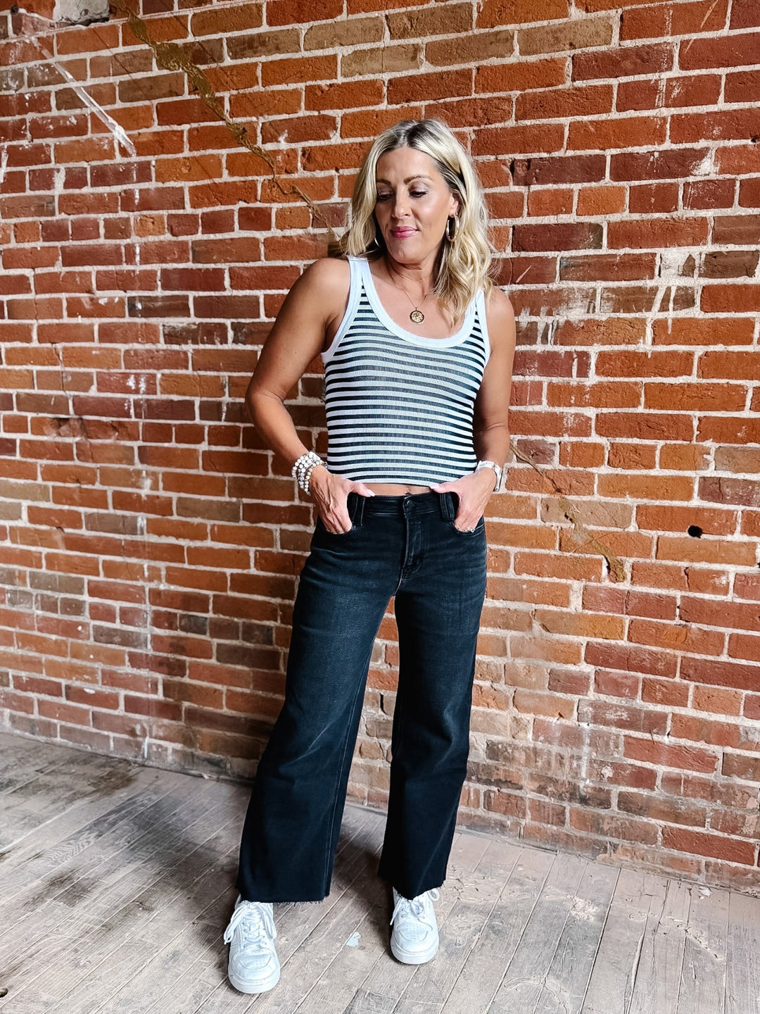 Woman wearing a white and black reversible stripe tank top, standing against a brick wall.
