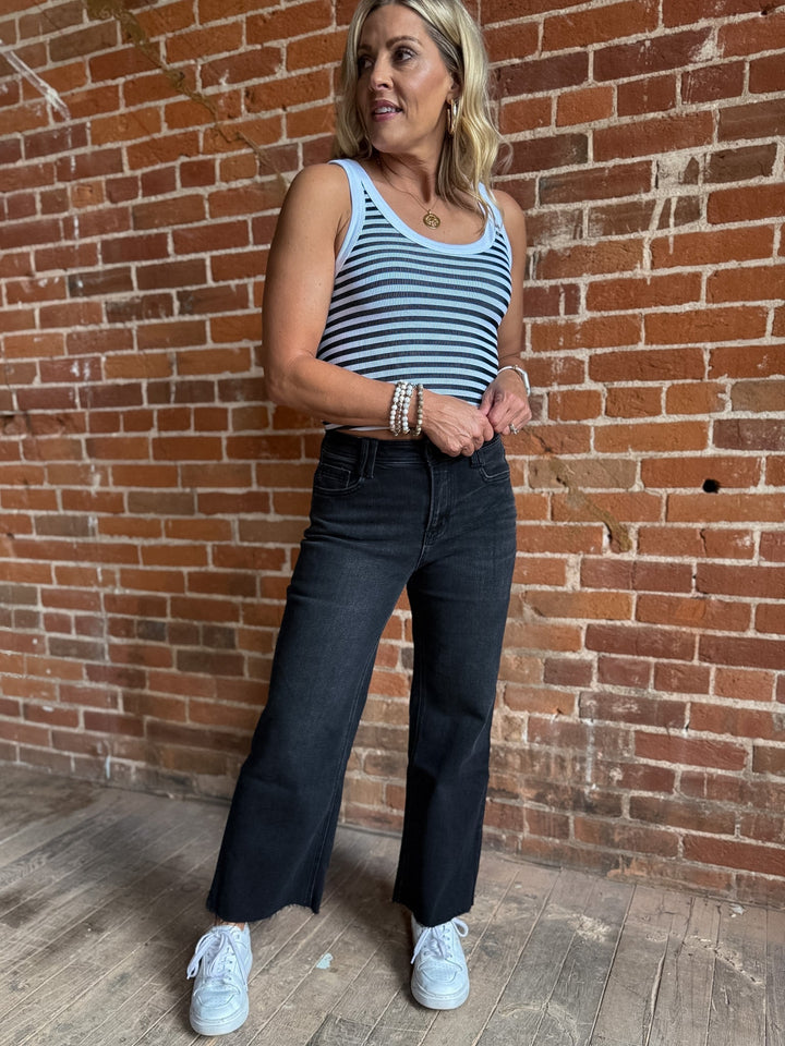 Woman wearing a white and black reversible stripe tank top, standing against a brick wall.
