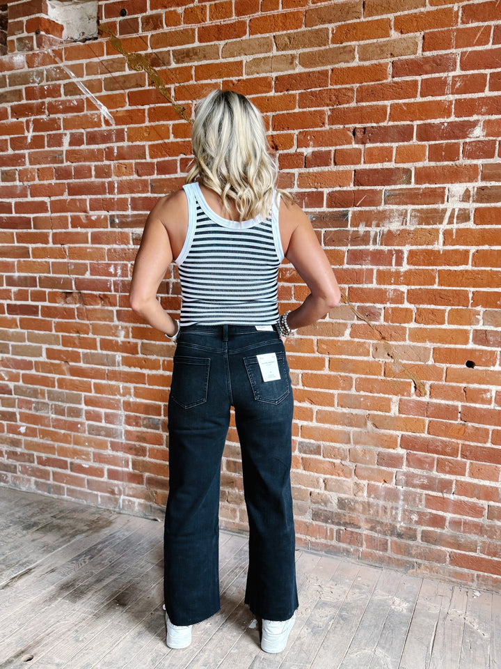 Woman wearing a white and black reversible stripe tank top, standing against a brick wall.