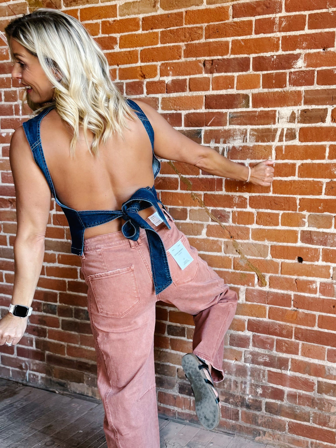 Woman wearing sleeveless dark denim top with open back and tie detail
