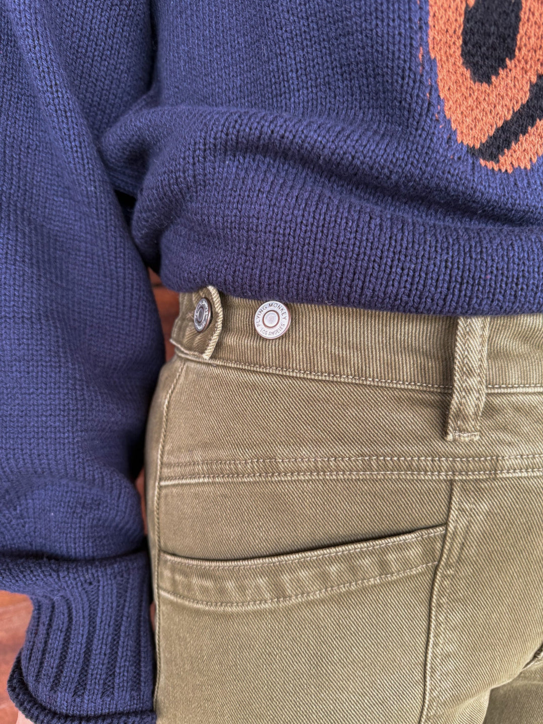 Close-up of a person wearing a navy blue knit sweater and olive green pants, focusing on the waistband with silver buttons.