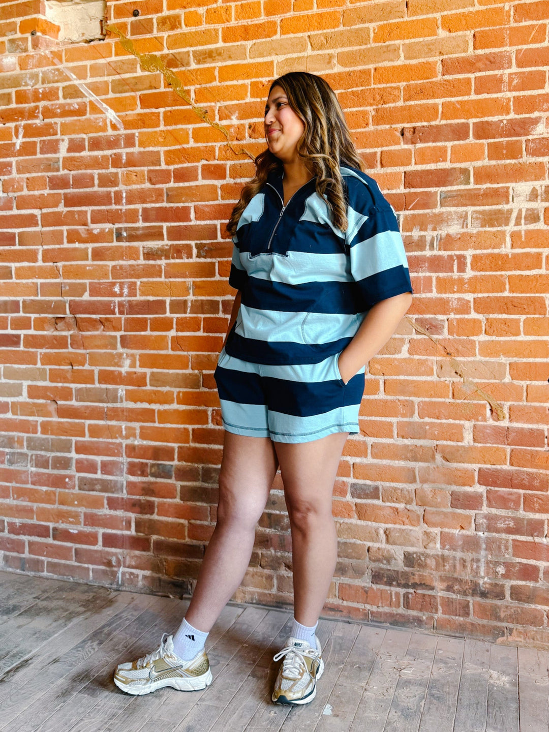A woman wearing a navy and sky blue striped set with an oversized top and shorts, standing against a brick wall.
