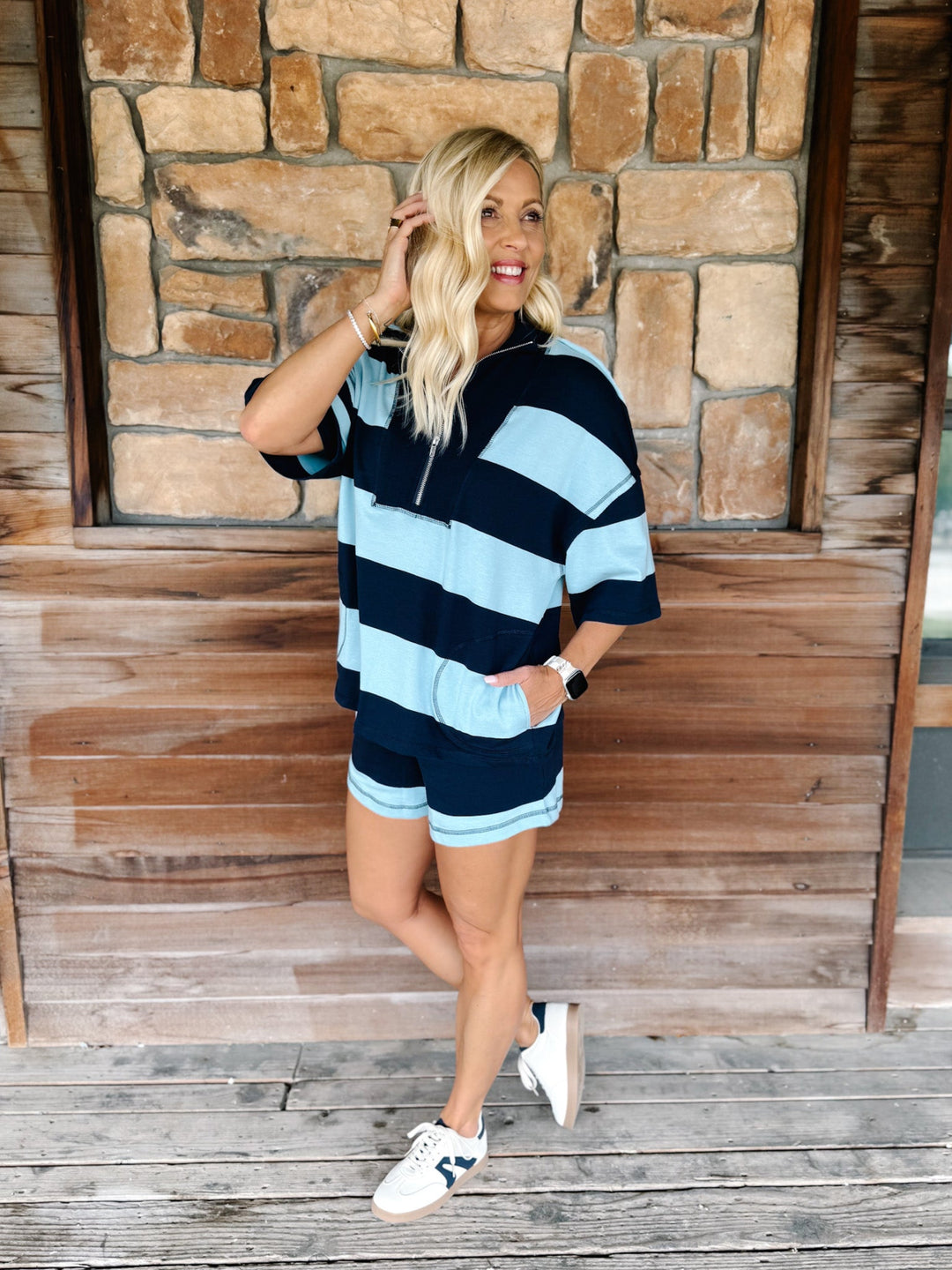A woman wearing a navy and sky blue striped set with an oversized top and shorts, standing against a brick wall.