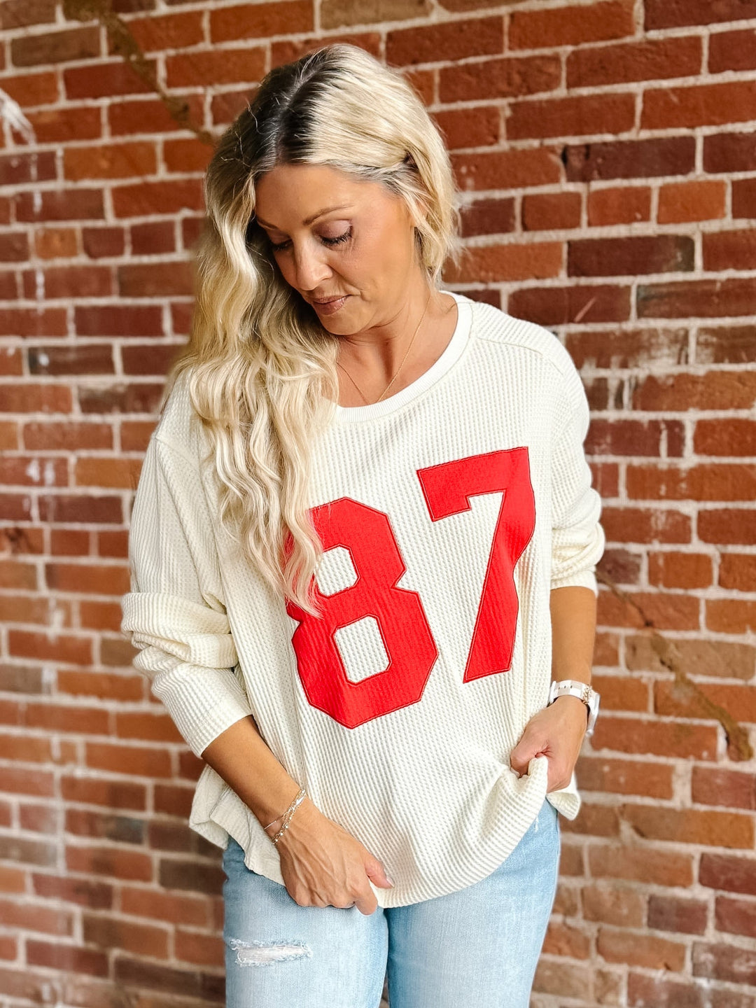 A woman wearing a cream ribbed knit sweater with a large red &
