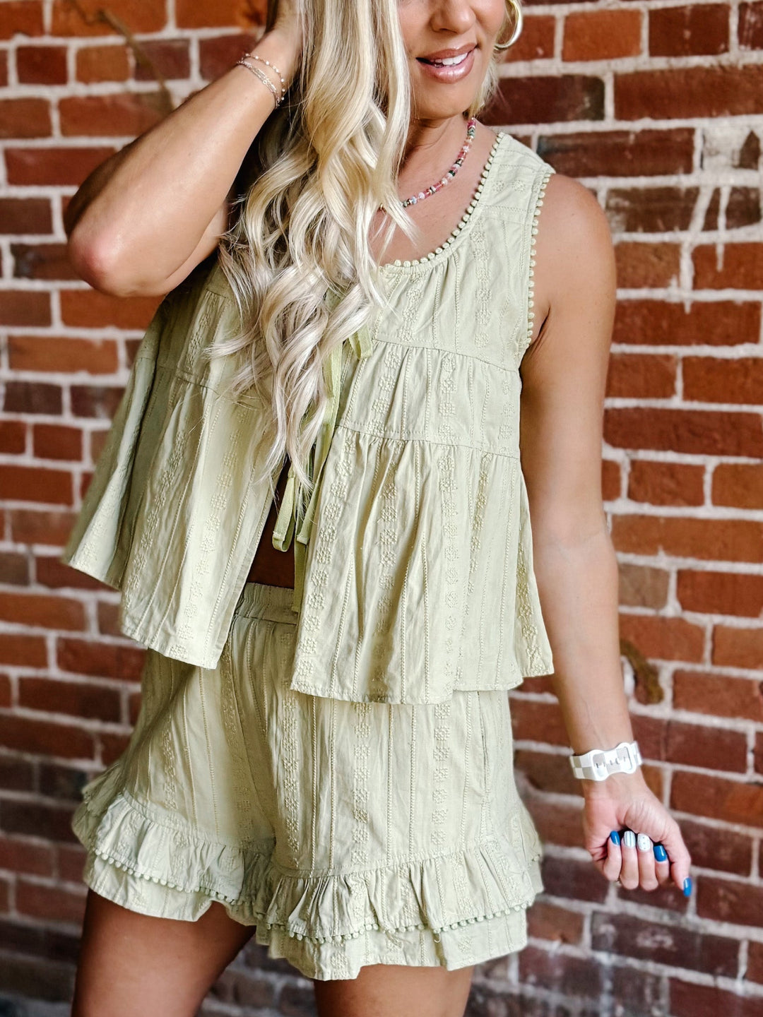 Two-piece set in willow green featuring a tiered babydoll top with pom pom trim and matching ruffle shorts with an elastic waistband.
