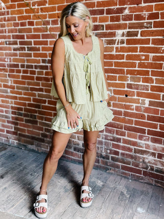 Two-piece set in willow green featuring a tiered babydoll top with pom pom trim and matching ruffle shorts with an elastic waistband.