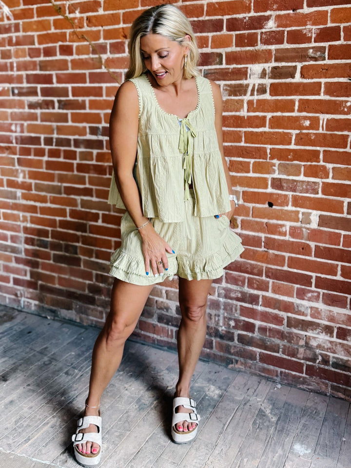 Two-piece set in willow green featuring a tiered babydoll top with pom pom trim and matching ruffle shorts with an elastic waistband.