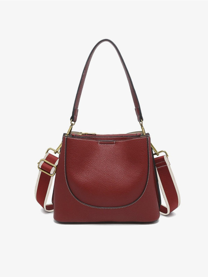 A burgundy pebbled leather handbag with a top handle, a curved front pocket, and a detachable shoulder strap with cream and burgundy sections, shown against a plain white background.