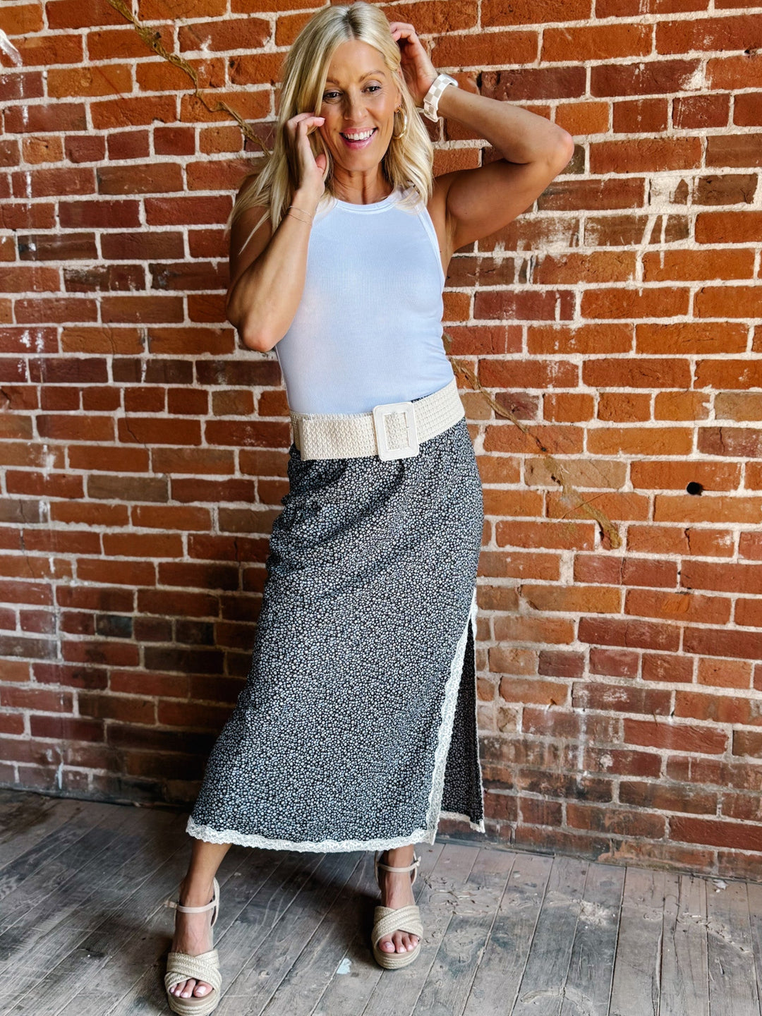 Ivory woven stretch belt with square buckle worn over floral skirt against brick wall.