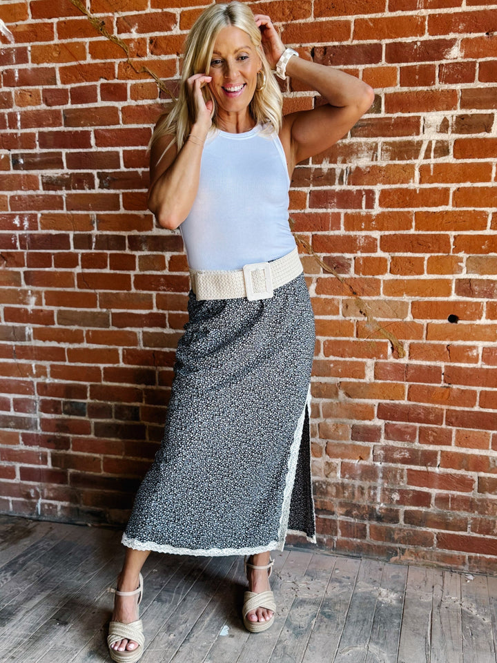 Ivory woven stretch belt with square buckle worn over floral skirt against brick wall.